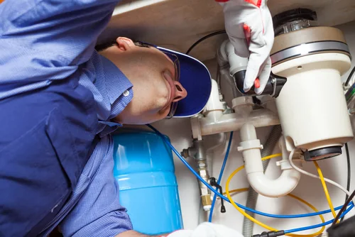 Technician servicing a garbage disposal beneath a kitchen sink