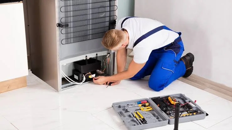 Technician checking components behind a household freezer